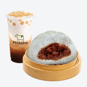 A glass of milkshake and a wooden bowl of siopao